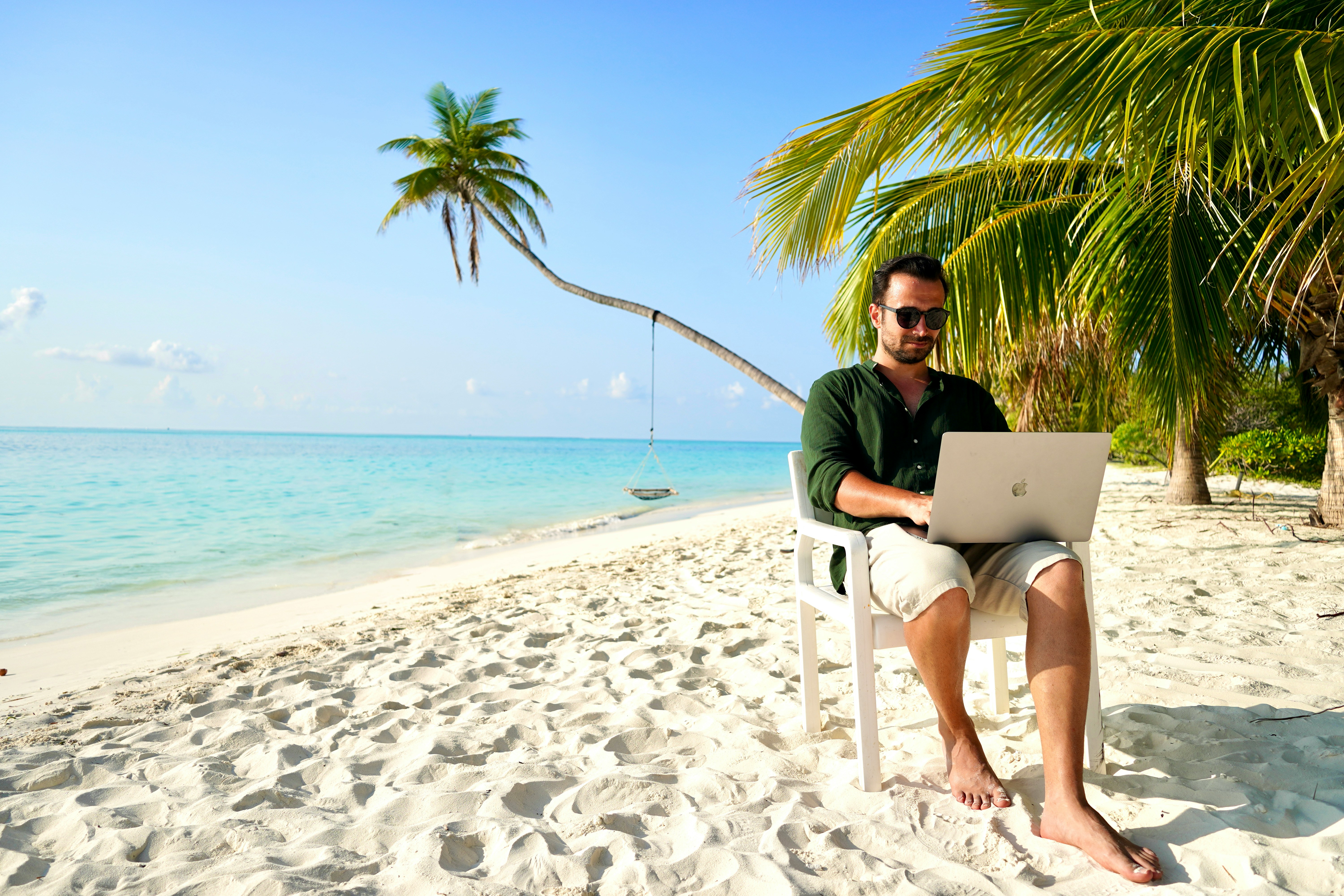 Newsletternameldung Man mit Laptop sitzt am Strand mit Palmen