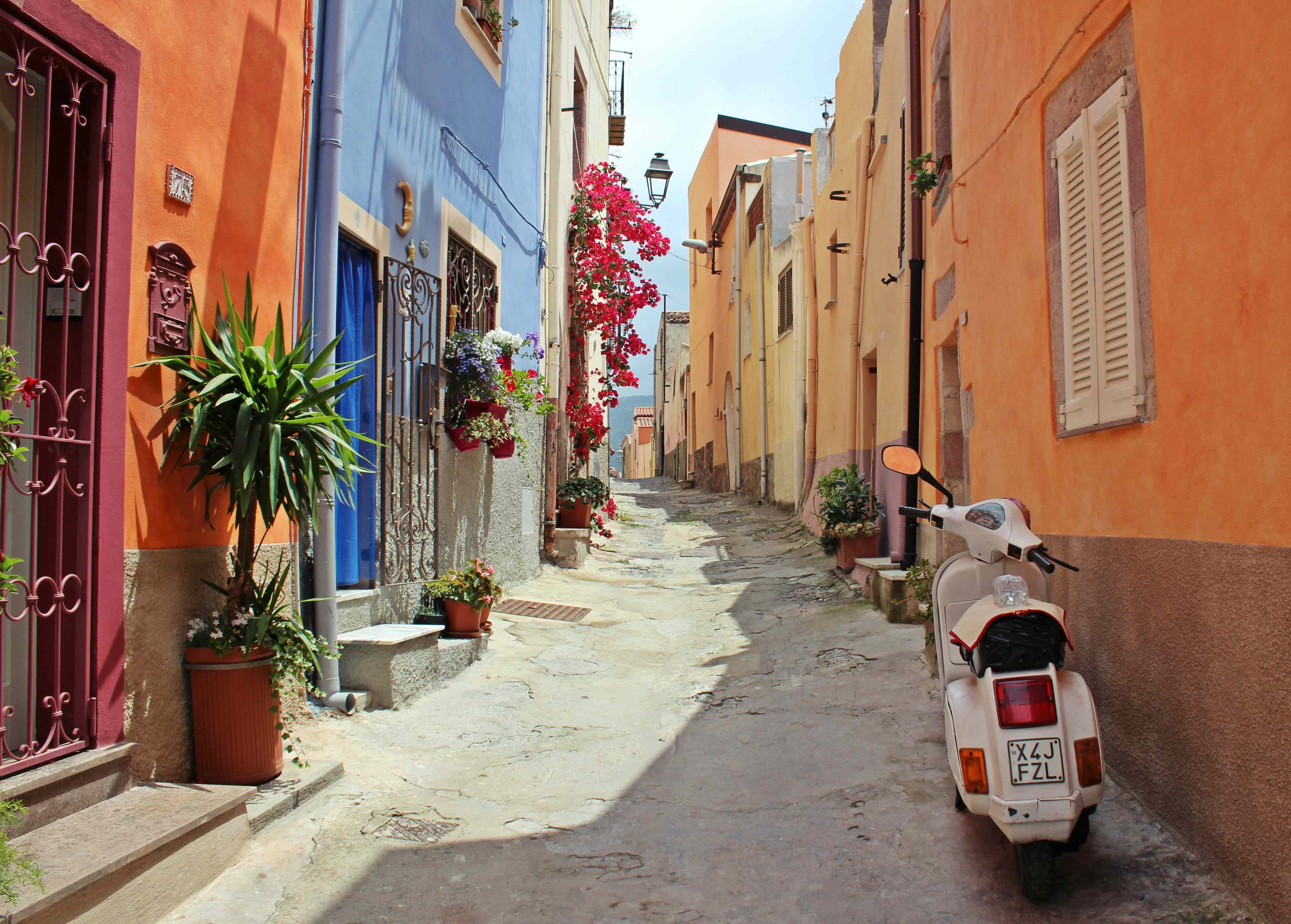 italien-rundreise Eine mediterrane Gasse mit bunten Häusern und einer Vespa.