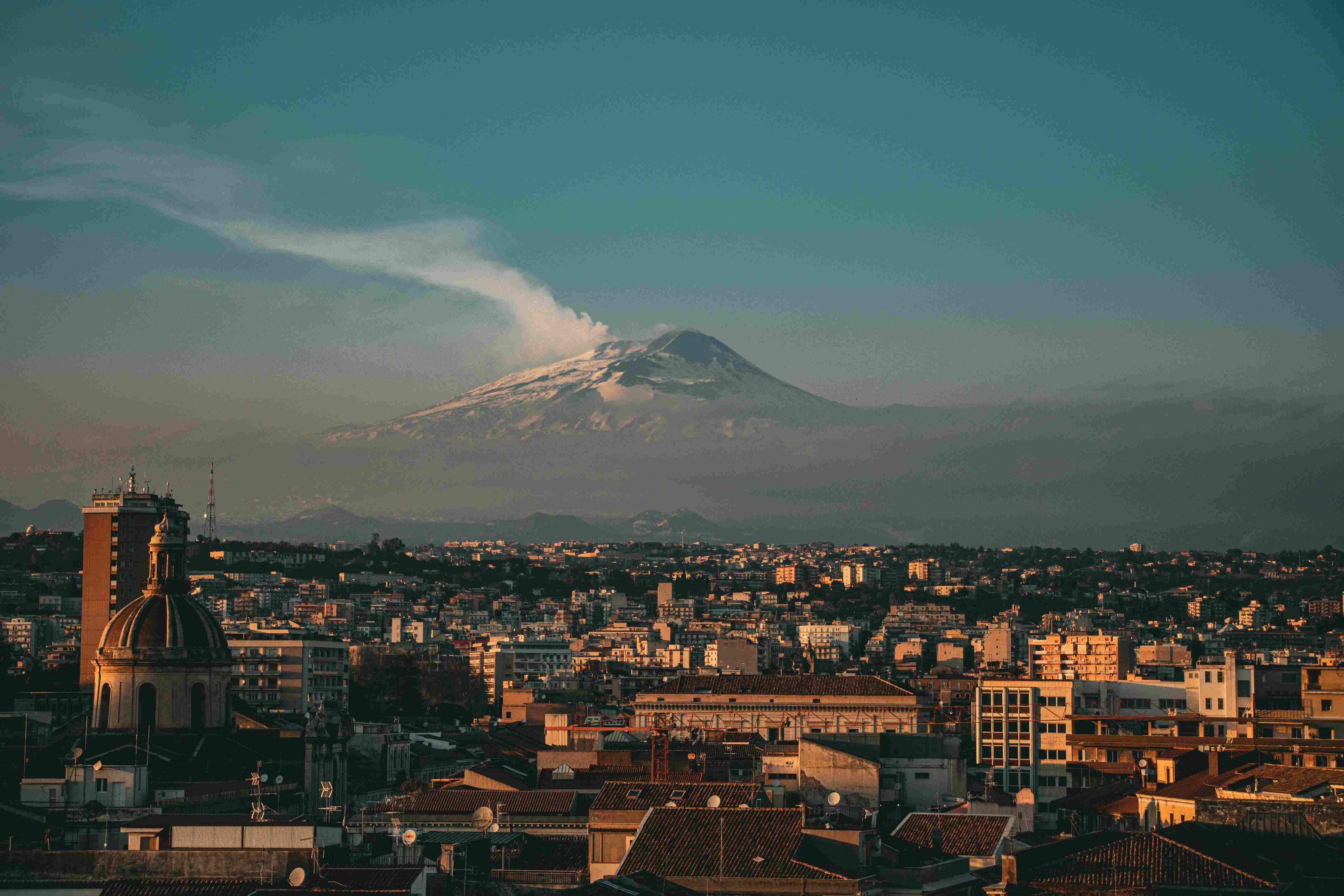 aetna-vulkan Eine italienische Stadt im Hintergrund der mit Schnee bedeckte, rauchende Ätna-Vulkan