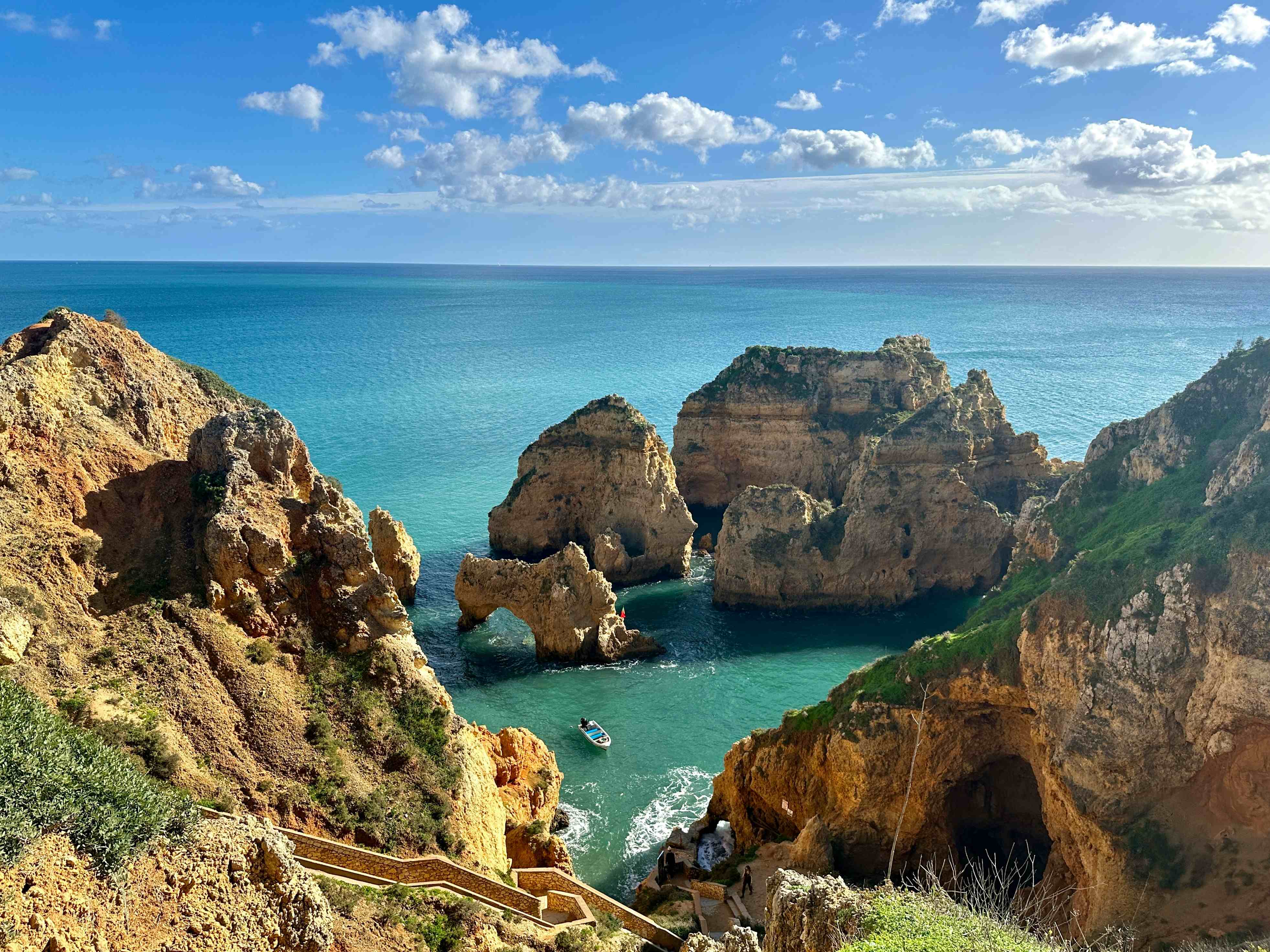 algarve-ganzjahresziel An einer steilen Klippe führt ein Weg herunter ans Meer. Auf dem Meer skurrile Felsformationen