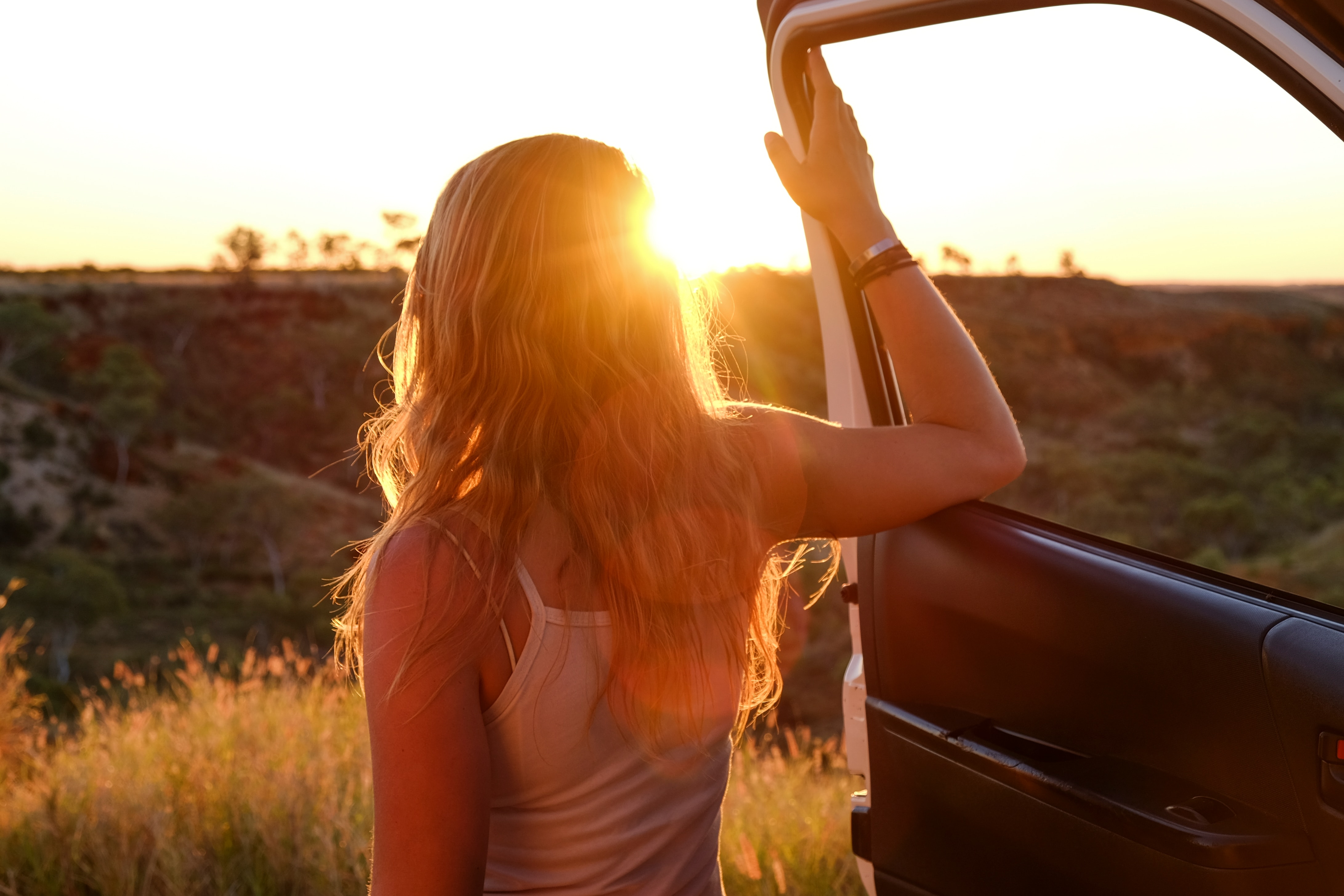 mietwagen-im-urlaub Eine junge Frau öffnen eine Autotür und blickt in den Sonnenuntergang