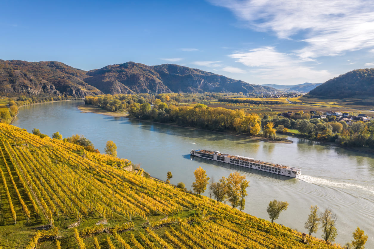 flusskreuzfahrten-herbst-winter Ein Flusskreuzfahrtschiff gleitet auf einem ruhigen Fluss durch eine herbstliche Weinregion