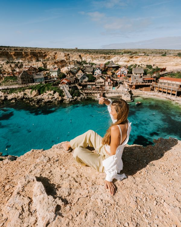 Besonders reisen - Eine junge Frau sitzt in sommerlicher Kleidung auf einem steilen Felsabhang und schaut in die Ferne. Unter ihr türkises, klares Meer. Eine junge Frau sitzt in sommerlicher Kleidung auf einem steilen Felsabhang und schaut in die Ferne. Unter ihr türkises, klares Meer.